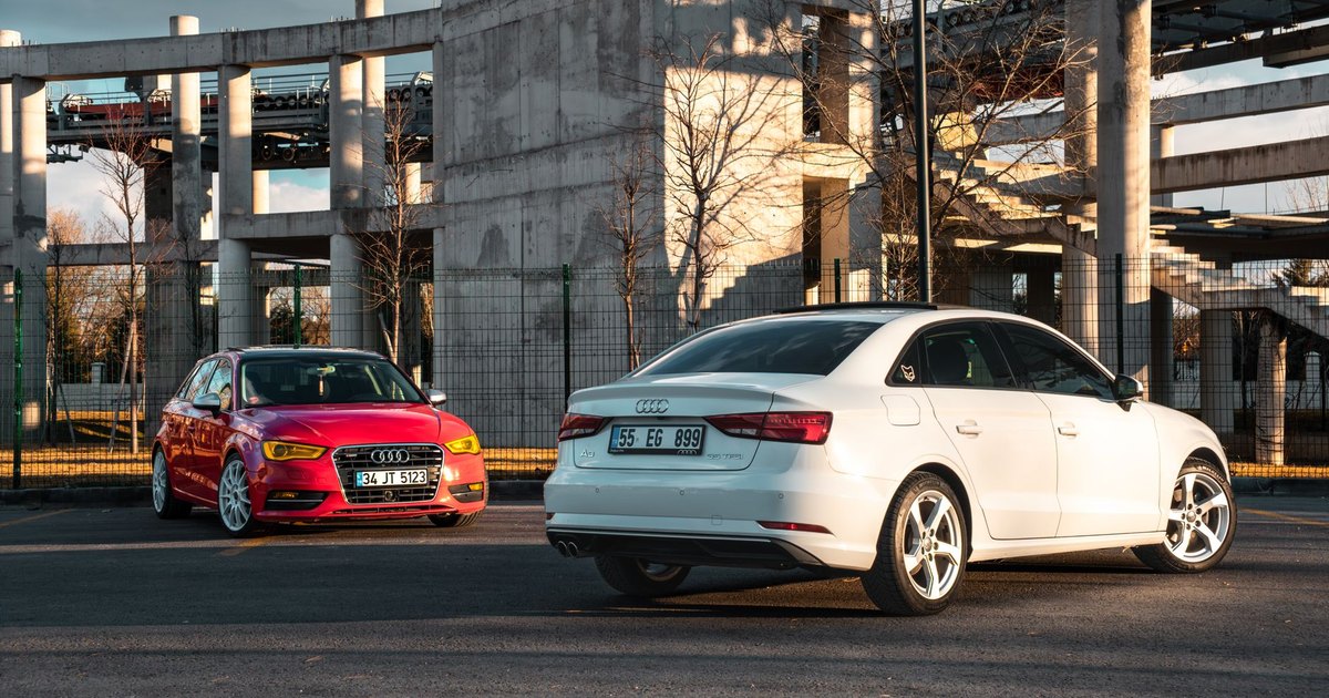 White and red Audi hatchbacks parked side by side against industrial architecture