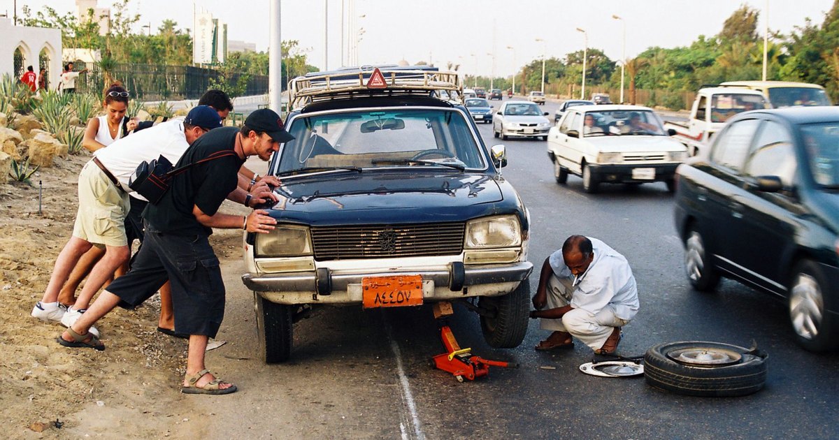 People helping to repair a car stopped at a busy roadside