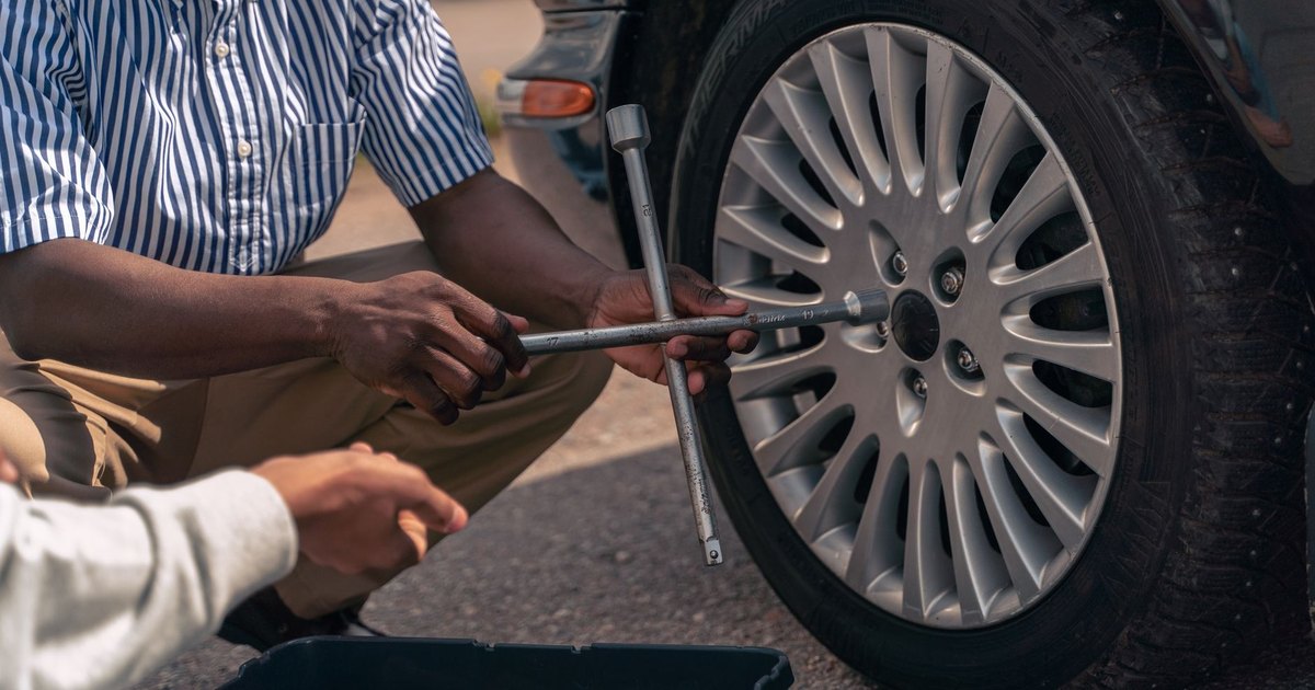 An adult showing a teenager how to change a wheel at the roadside