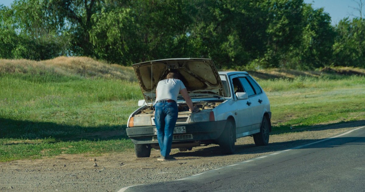 A driver standing beside a car at the roadside, inspecting a problem