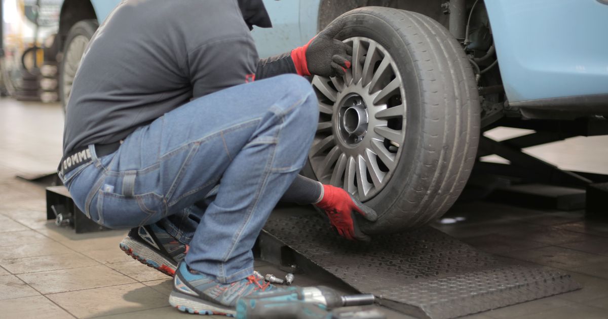 Technician changing a car tyre safely on level ground with the handbrake on