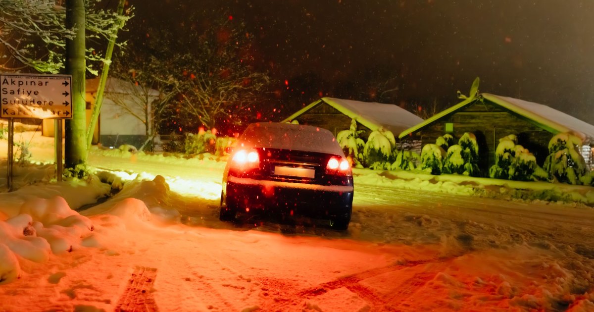 Car with glowing tail lights on a snow-covered road at night