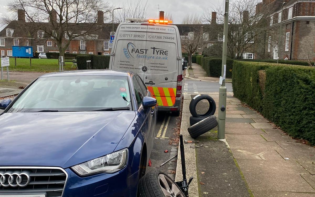 A blue Audi on a suburban street with the wheel off and the van behind