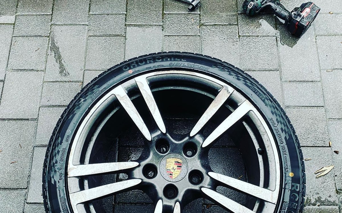 A Porsche alloy wheel on the pavement with the tools laid out beside it, serving Baldock, Hertfordshire